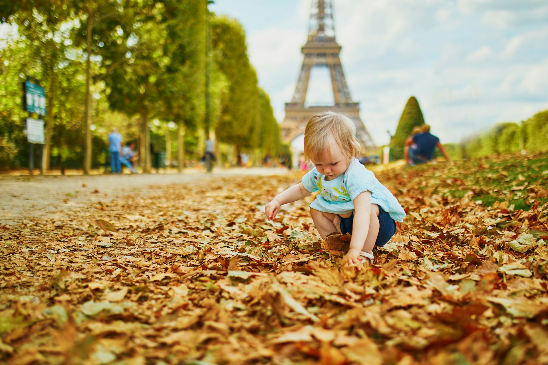 An adorable blond toddler girl plays with fallen autumn leaves near the Eiffel Tower in Paris, France